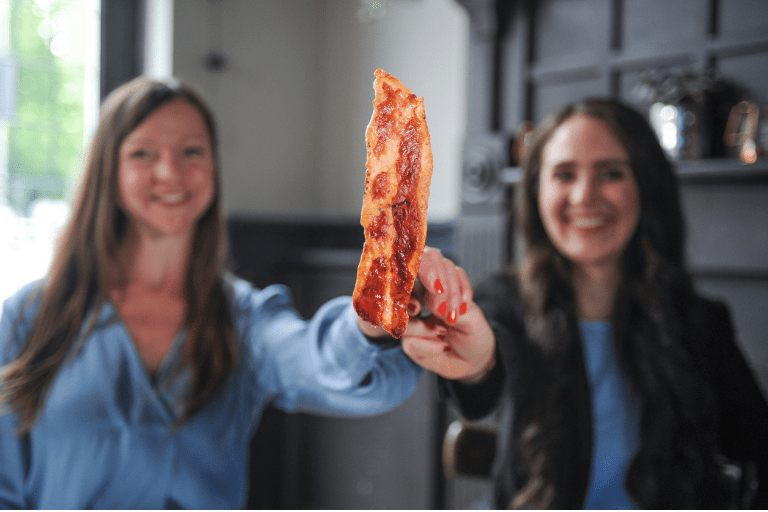 Dve ženy držia slaninu od Higher Steaks a Tailored Brands, vyrobenú kultiváciou zvieracích buniek.